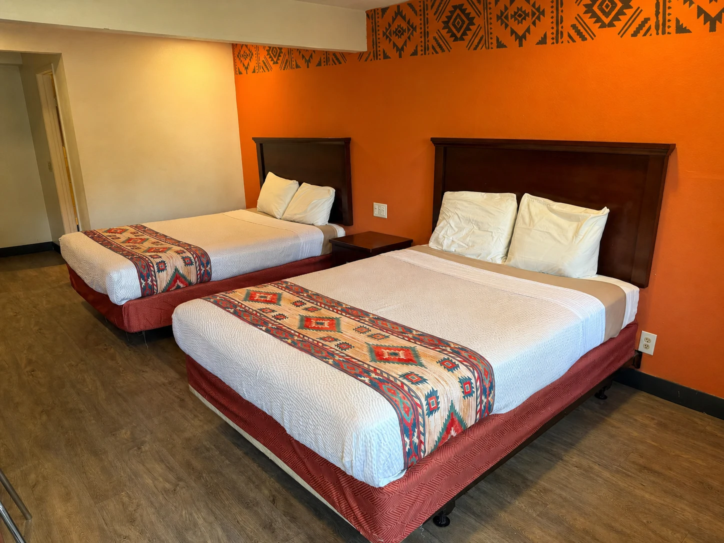 Spacious room with two queen beds and a hand-painted geometric border on the orange accent wall